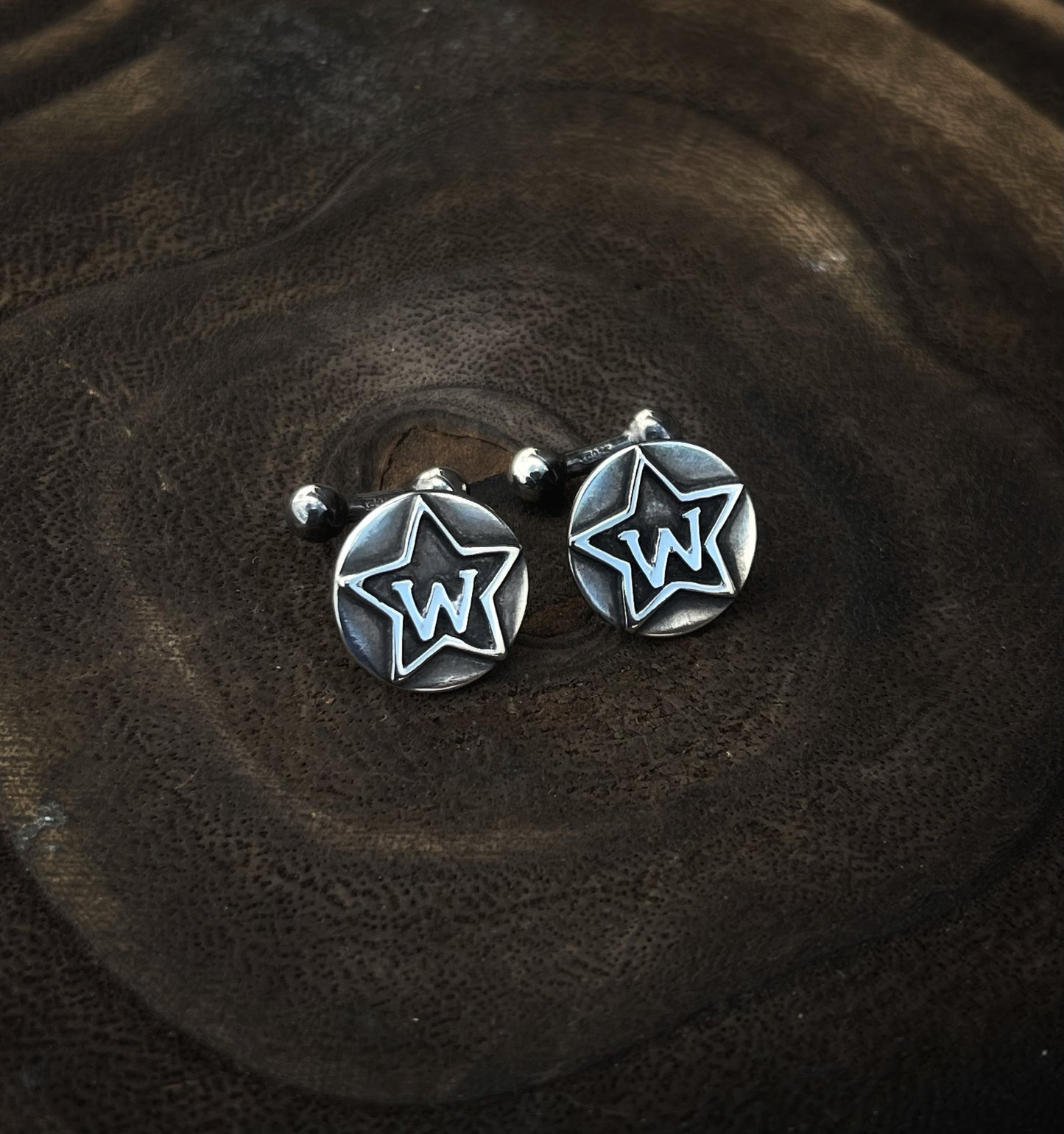 Sterling Silver cufflinks with silver brand overlayed. On a wood background. 